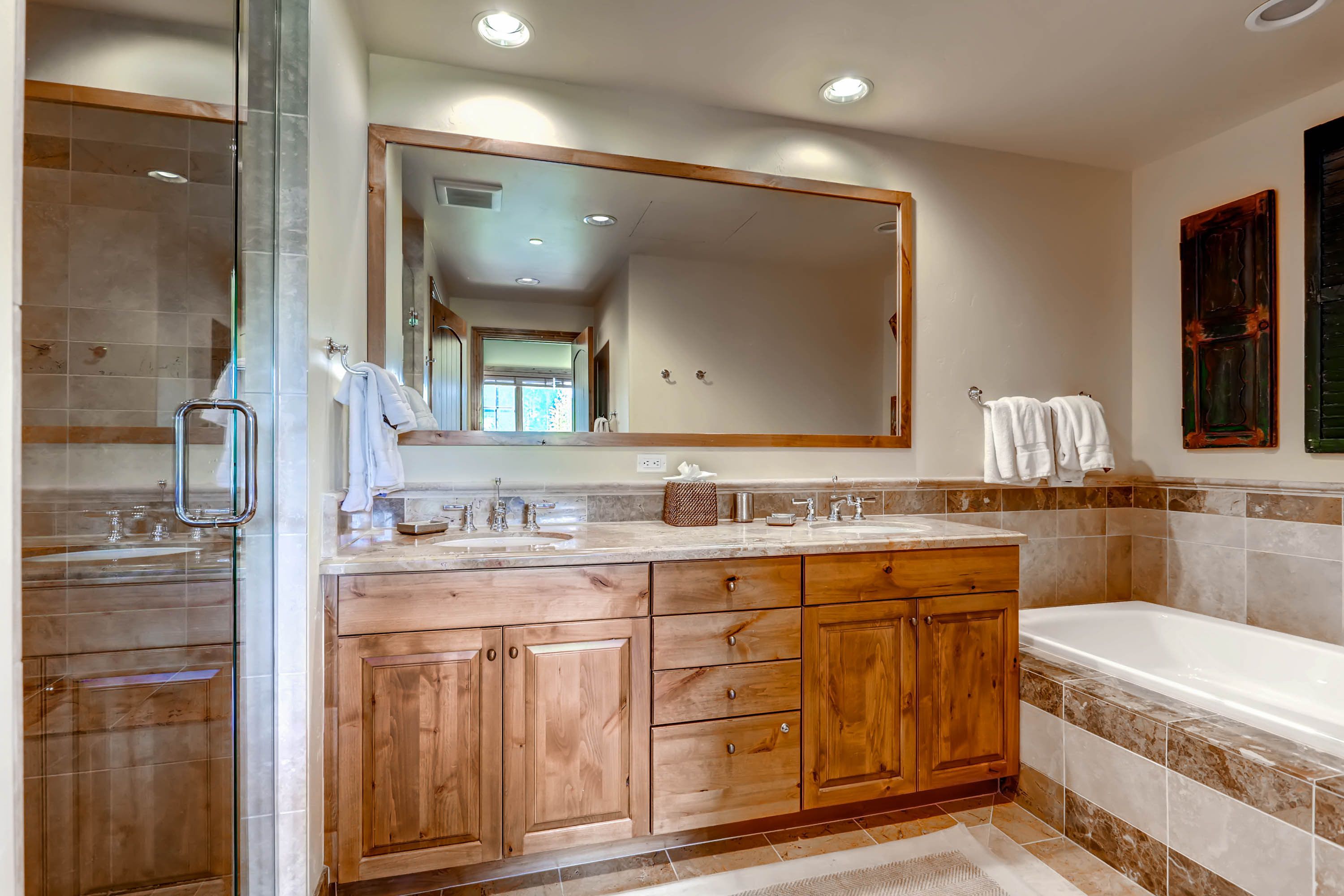 A modern bathroom with a glass shower enclosure, wooden vanity, and a large mirror.