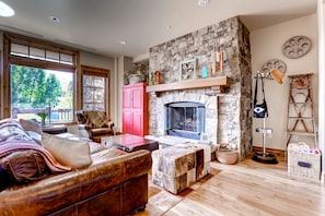 A cozy living room with a stone fireplace, leather furniture, and a large window offering a view of trees.