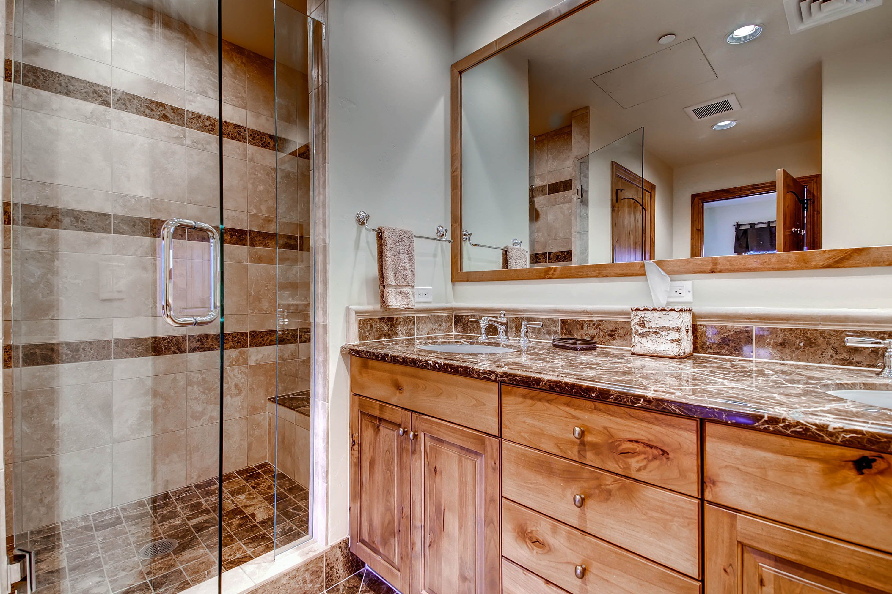 Un baño con cabina de ducha de vidrio, tocador de madera con encimera de mármol y un espejo grande sobre el lavabo.