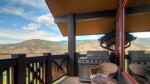 Ein Balkon mit Korbstühlen, einem Grill und Blick auf die Berge.
