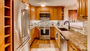 A modern kitchen with wooden cabinets, stainless steel appliances, a stone backsplash, and a granite countertop.