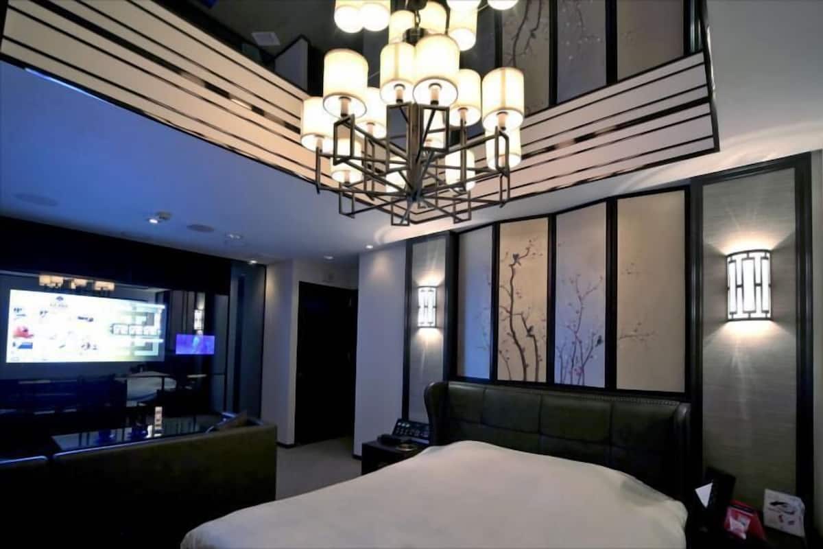 A modern hotel room with a large bed, a TV, a desk, and a unique chandelier.