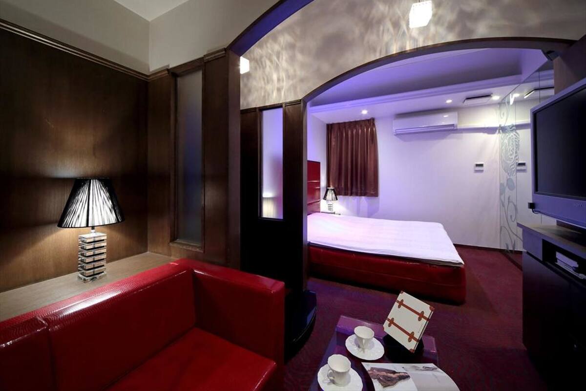 A hotel room with a red sofa, a bed, a TV, and a small table with cups and a menu.
