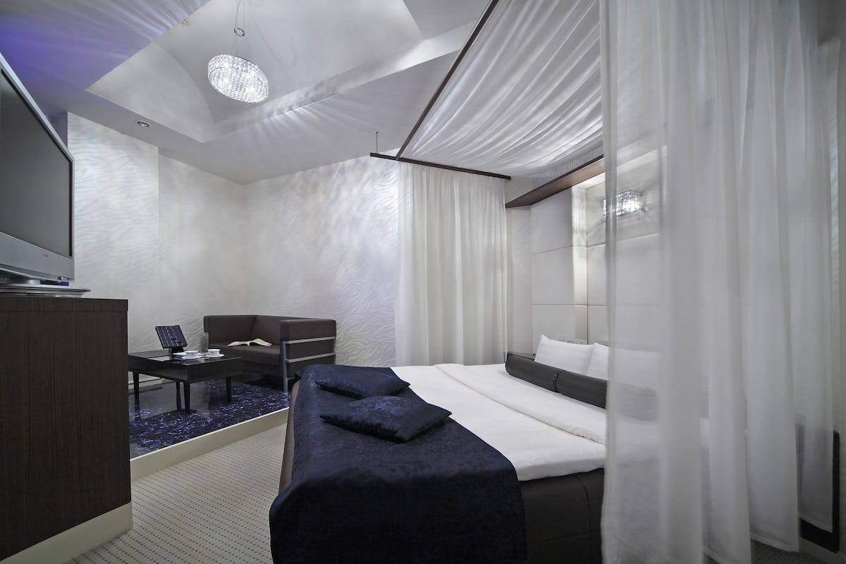 A modern hotel room with a bed, a desk, a chair, and a television.
