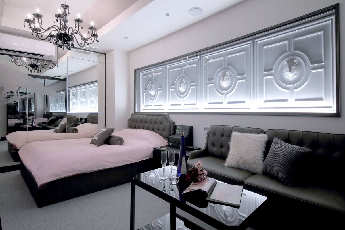 A modern bedroom with a large bed, a sofa, a glass coffee table, and a wall-mounted light fixture.