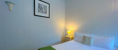 Een net opgemaakt bed met wit en groen beddengoed, een ingelijst kunstwerk aan de muur en een bedlampje.