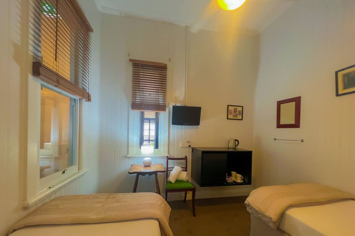 Habitación de hotel con dos camas, una mesita con una silla, televisión y una estantería con hervidor y tazas.