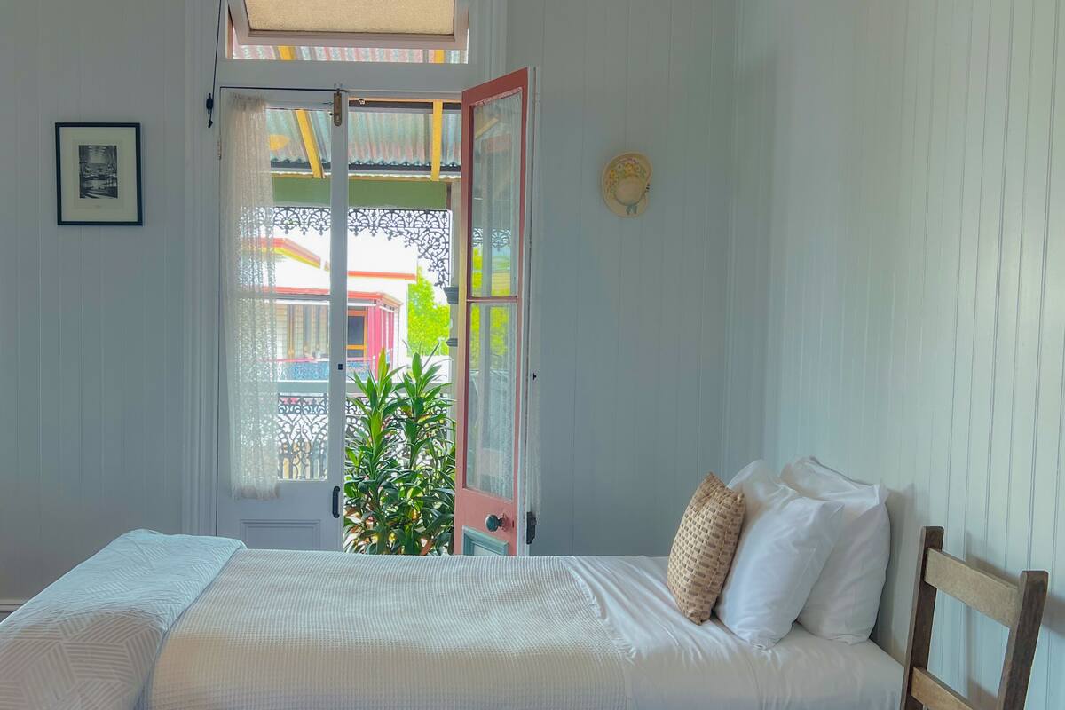 Un dormitorio con una cama, una silla de madera, una planta en maceta y una puerta que da a un espacio exterior.