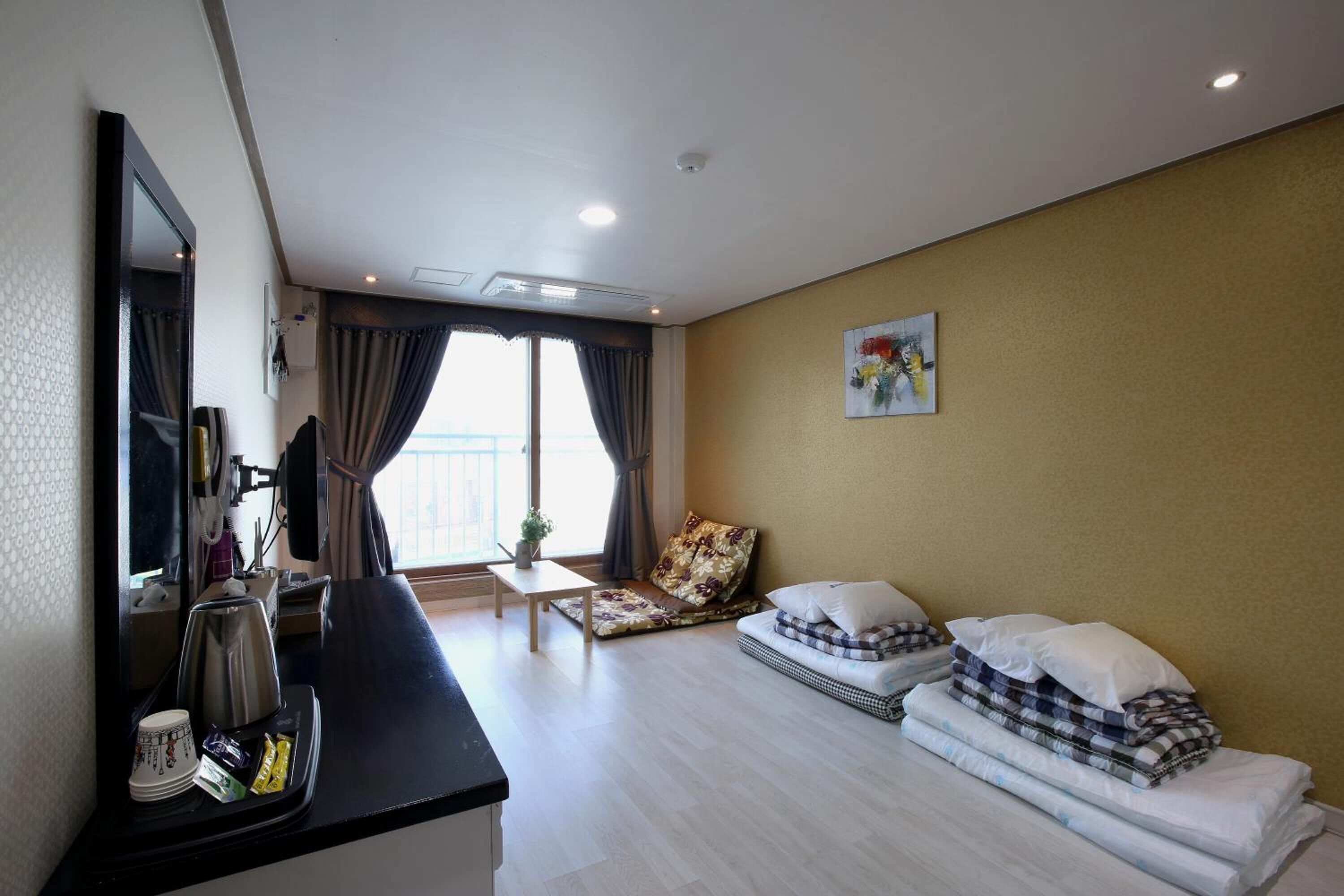 A hotel room with a bed, a desk, a chair, a large window, and a painting on the wall.