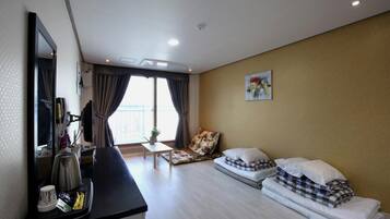 A hotel room with a bed, a desk, a chair, a large window, and a painting on the wall.
