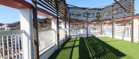 Une terrasse sur le toit dotée d’une structure de pergola en métal, d’un revêtement de sol en gazon synthétique et de garde-corps blancs.