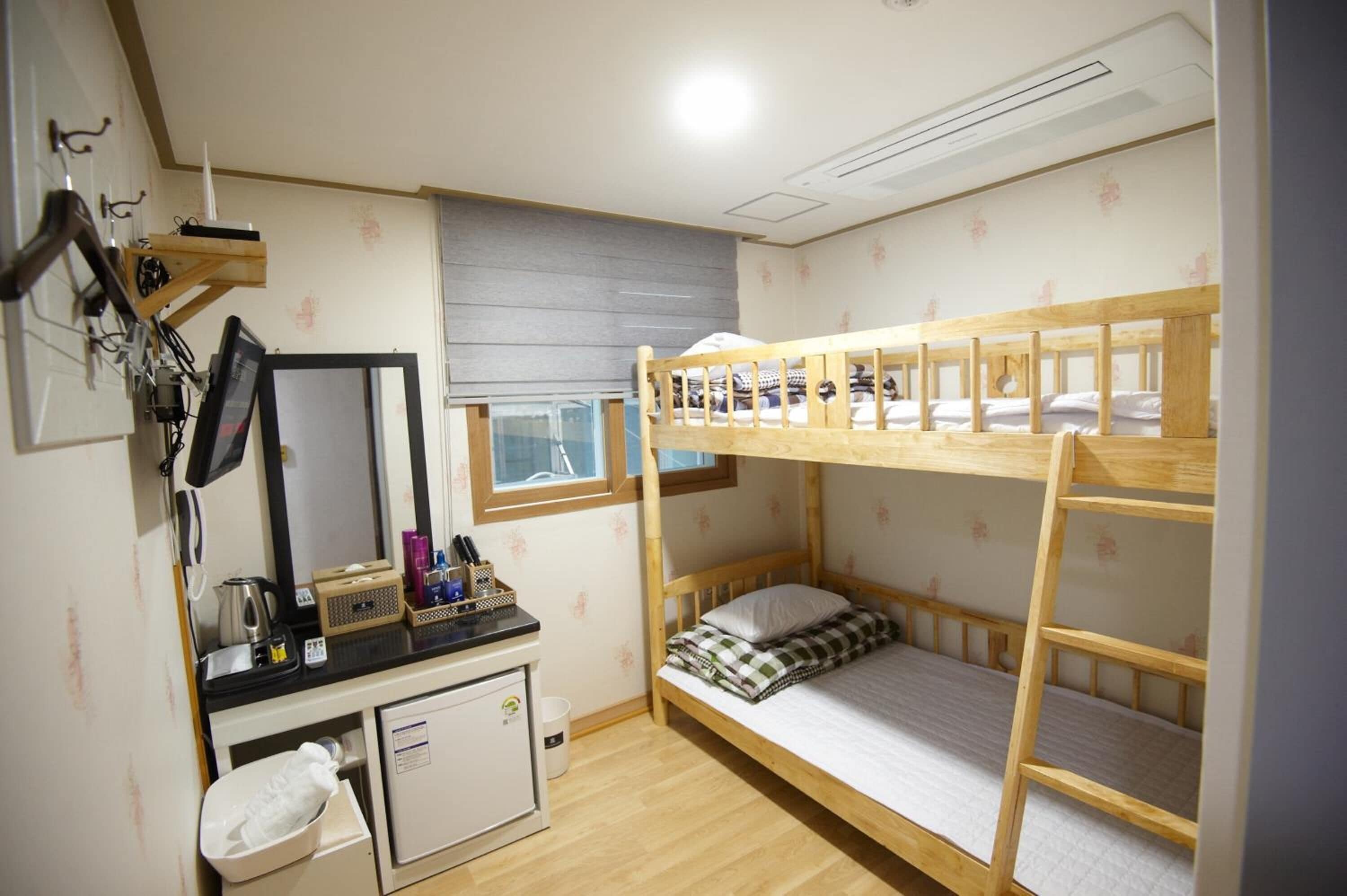 A bunk bed room with a desk, mirror, and a window.
