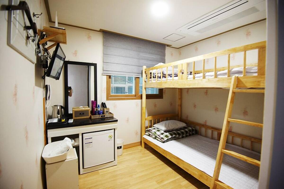 Een kleine, compacte kamer met een stapelbed, een bureau met spiegel en een kleine koelkast.