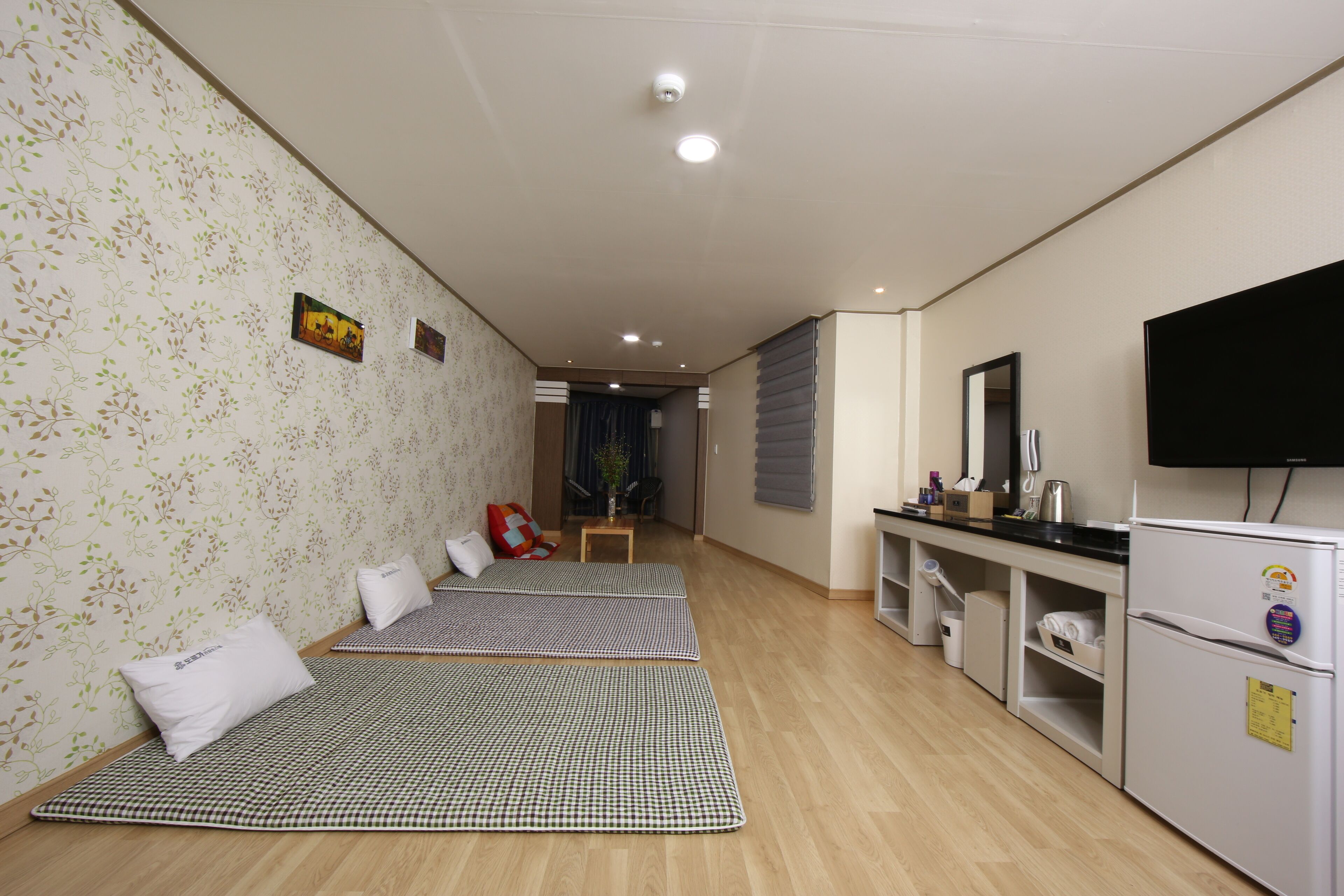 A hotel room with a checkered floor mat, a bed, a TV, a refrigerator, and a small table with a plant.