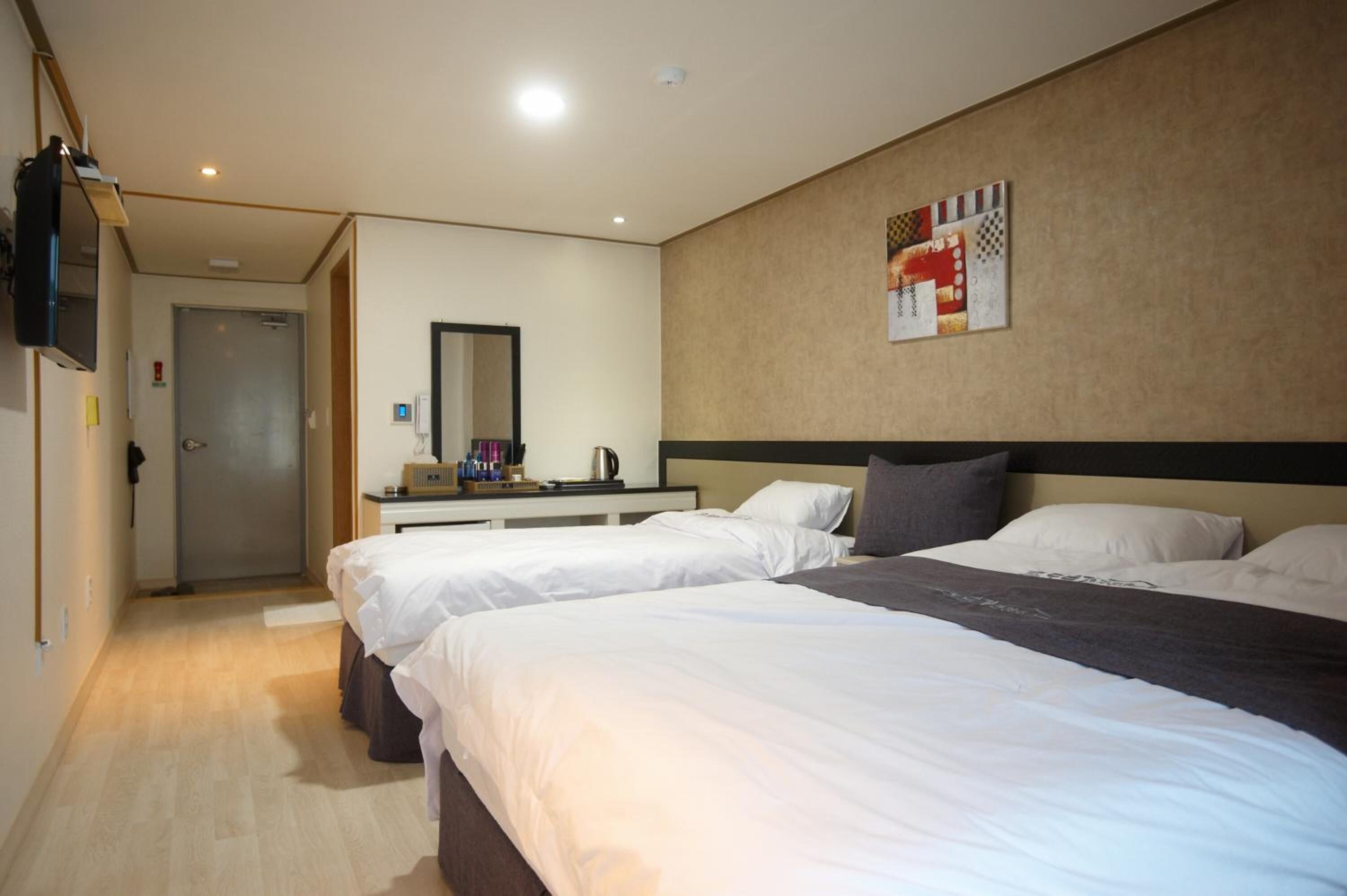 Une chambre d’hôtel avec deux lits, un bureau, un miroir et un téléviseur fixé au mur.