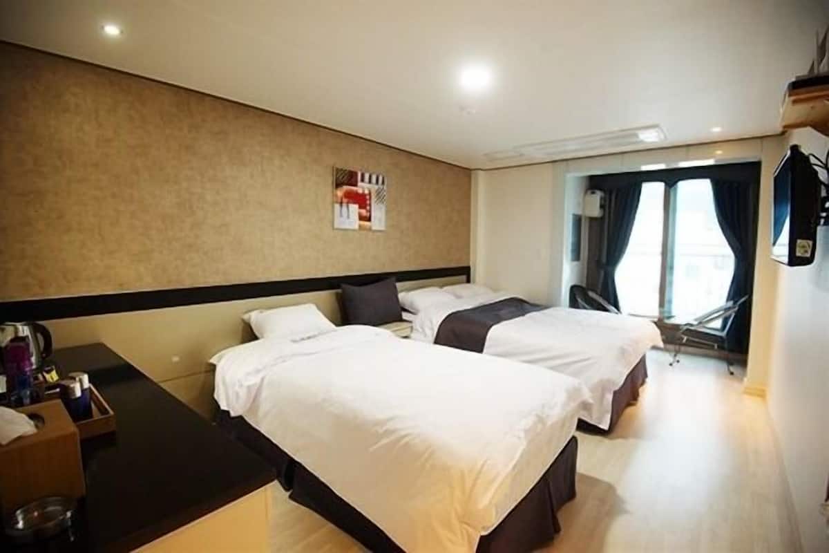 Een hotelkamer met twee bedden, een bureau met stoel, een klein tafeltje met waterkoker en een raam met gordijnen.
