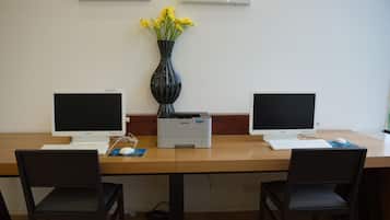 A workspace with two monitors, a printer, and a vase with yellow flowers on a wooden table.