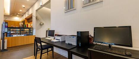A modern office space with a desk, computer, and printer. There is a window with blinds and a view of a store in the background.