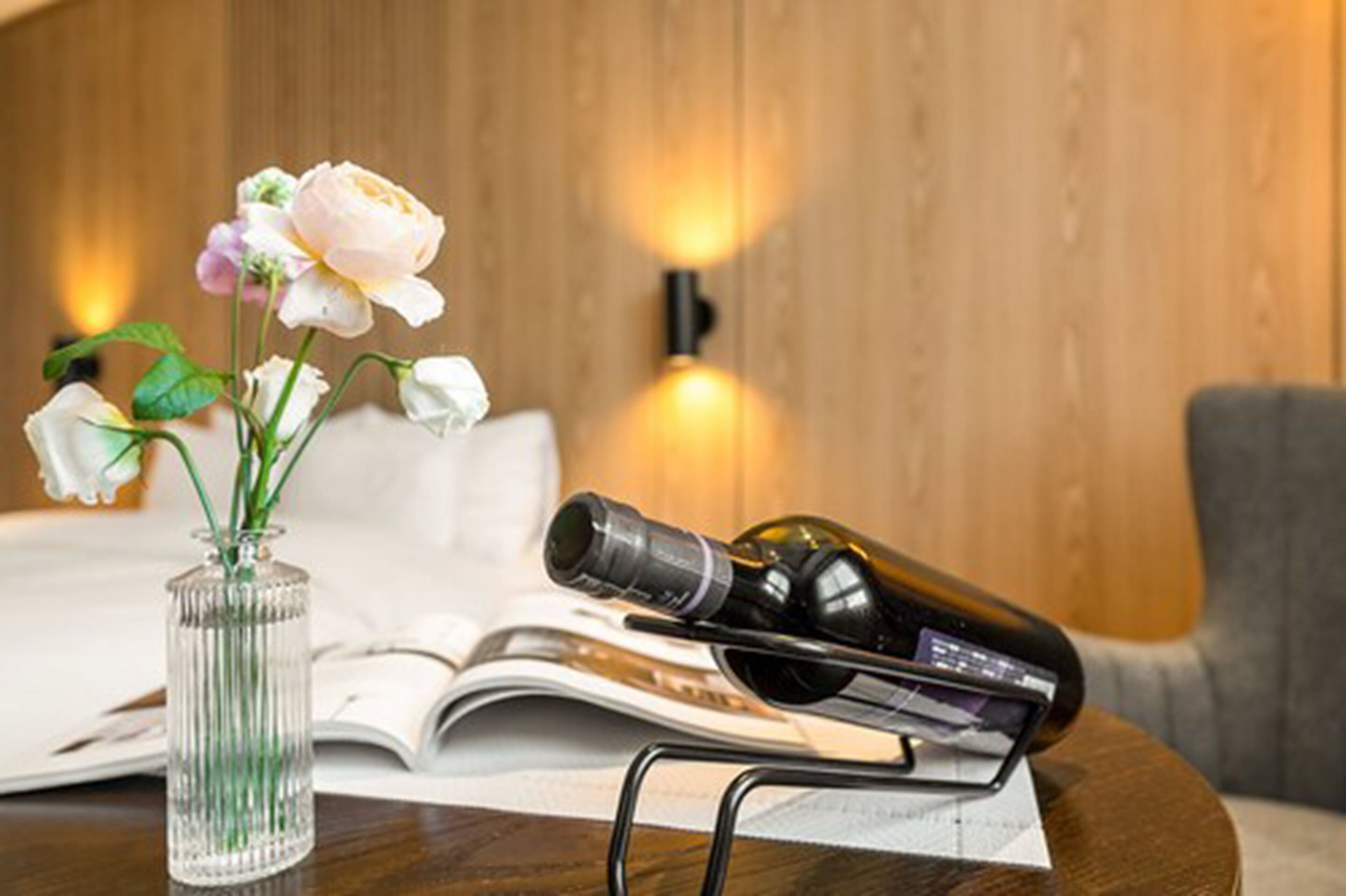 A wooden wall with a vase of flowers and a wine bottle on a table.
