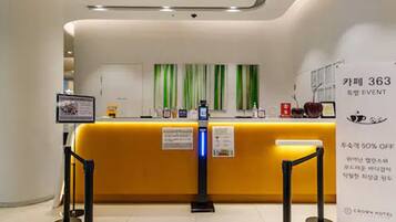 Ein Hotel-Rezeptionsbereich mit einem gelben Empfangstresen, einer digitalen Check-in-Kiosk und einem Schild, das auf ein 50%-Rabatt-Event hinweist.