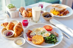 Une table de petit-déjeuner avec des croissants, des œufs, du bacon, des tomates et diverses confitures.