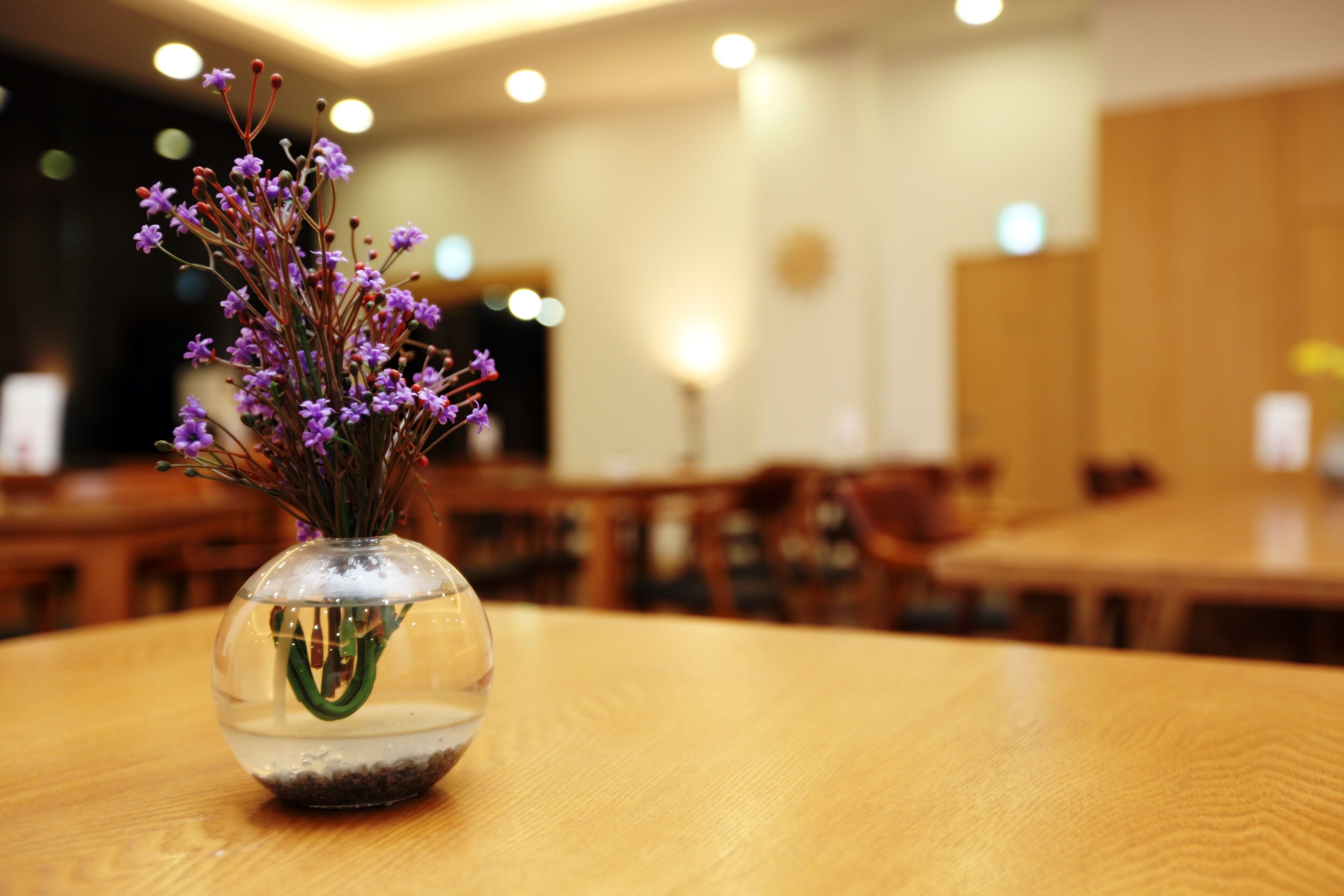 Een helder zicht op een ronde houten tafel met een glazen vaas met paarse bloemen.