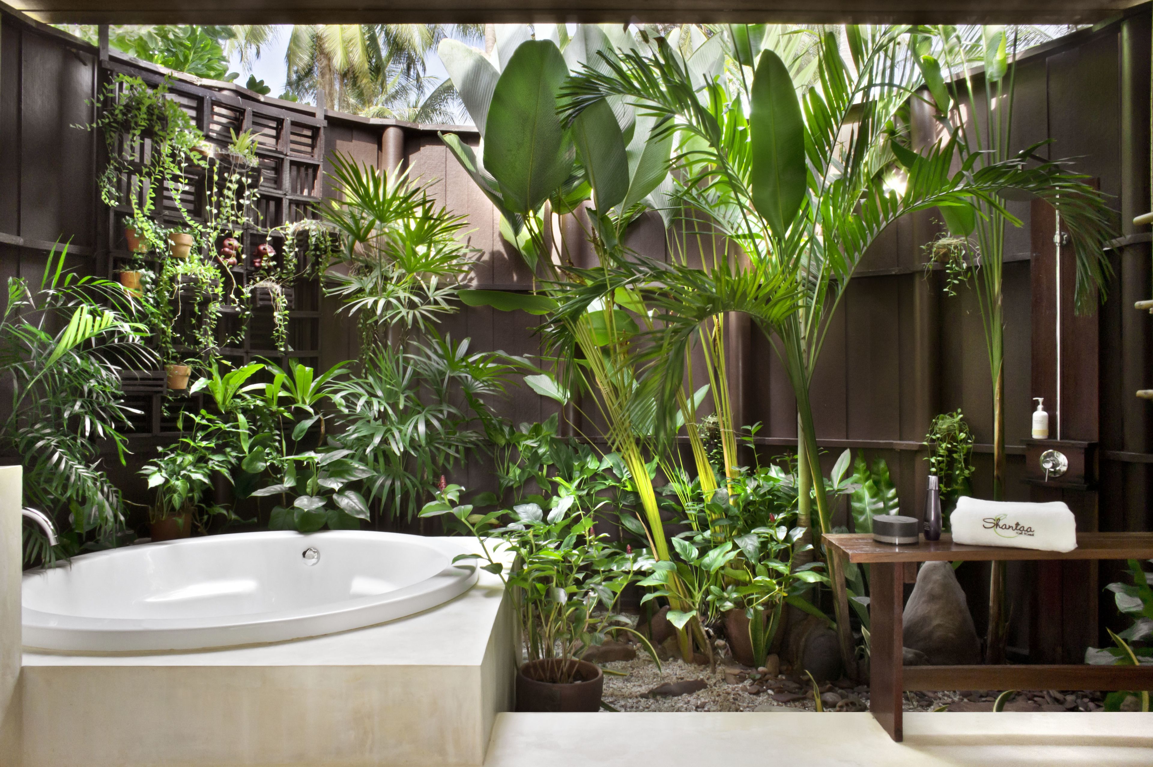 A spa area with a large bathtub, surrounded by lush tropical plants and a wooden fence.