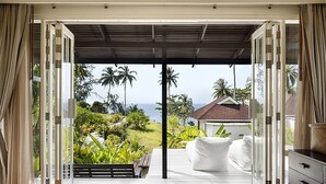 A room with a large sliding glass door leading to a deck with a view of the ocean and palm trees.