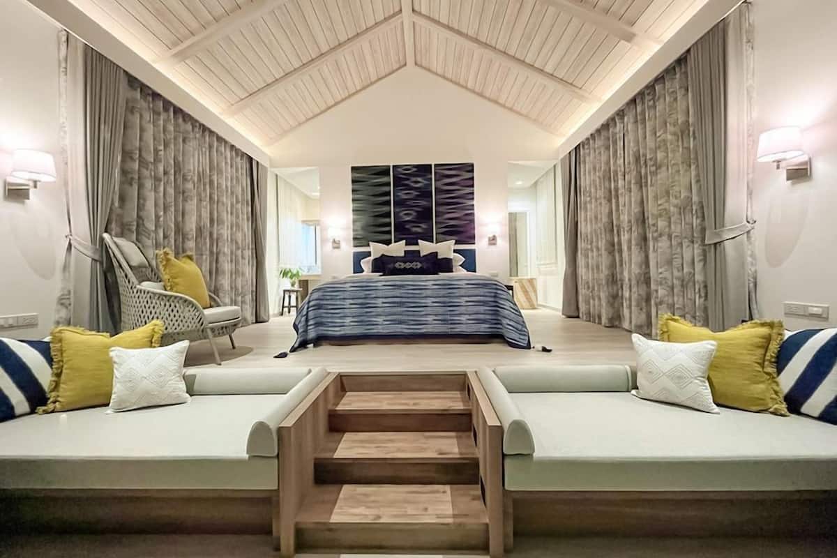 Un dormitorio moderno con una cama grande, dos sofás, una escalera y un techo con vigas de madera.