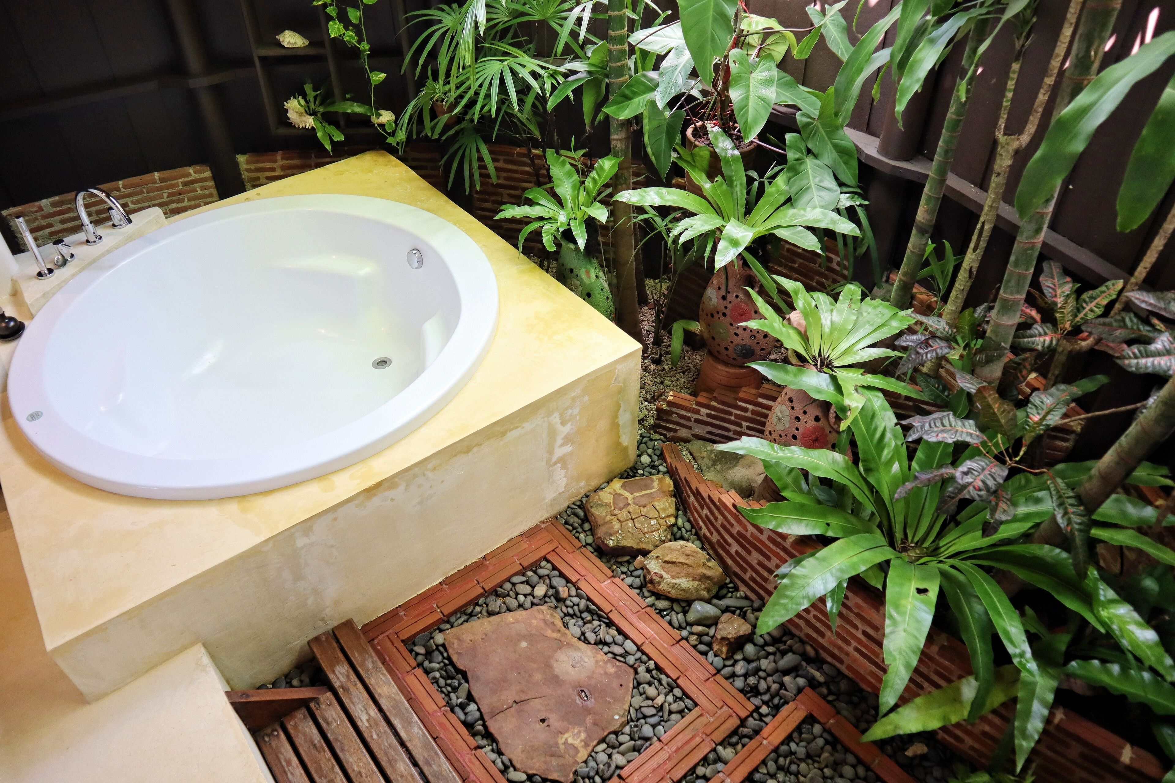 Un baño con una bañera grande, rodeado de diferentes plantas y un pequeño banco de madera.