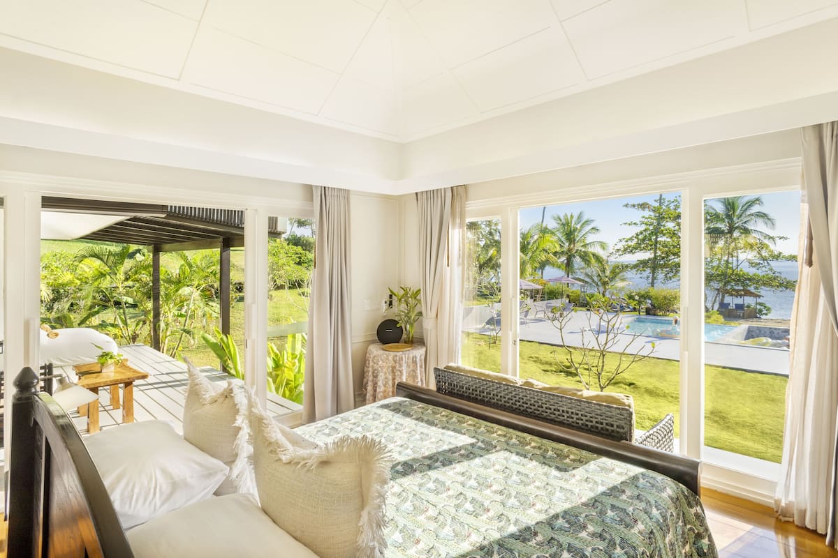 Un dormitorio con una cama grande, vistas a una piscina y vegetación.
