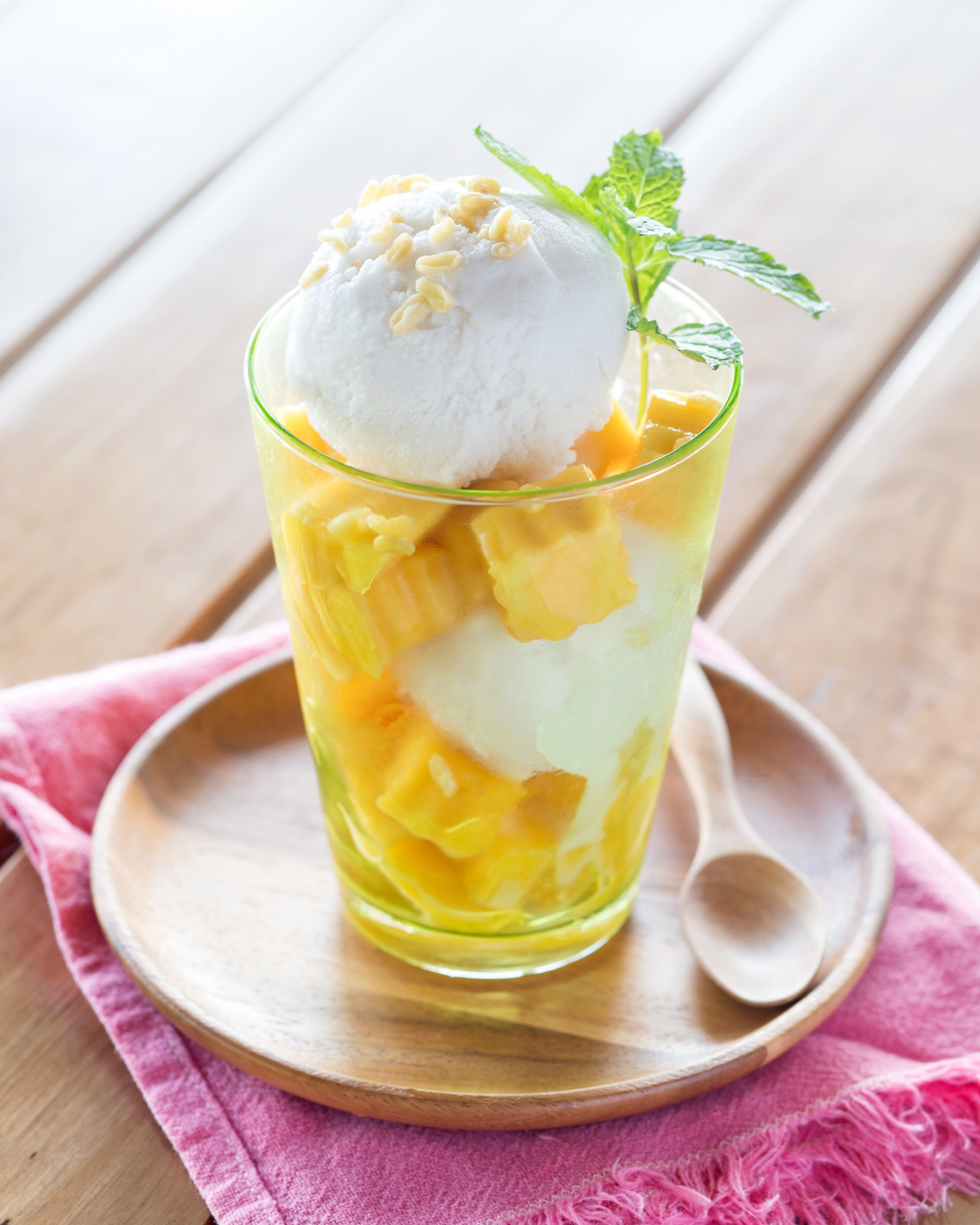 A glass dessert with mango chunks and a scoop of ice cream on a wooden spoon.