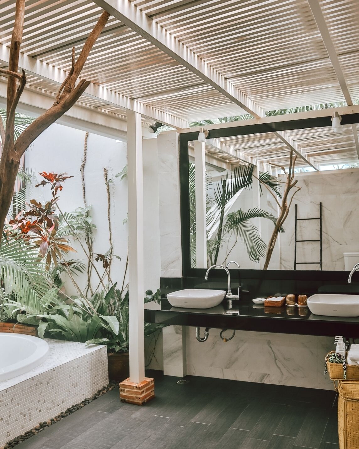 Un baño moderno con un espejo grande, dos lavamanos, una bañera y un techo con listones de madera.