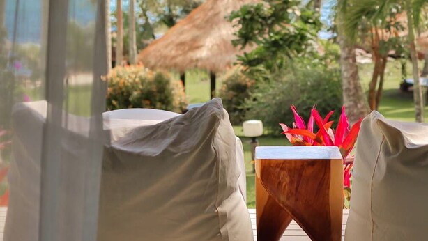 A view from a hotel room overlooking a beach with palm trees and a thatched-roof structure.