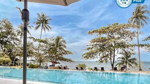Zona junto a la piscina con cojines a rayas, una tumbona y una palmera.