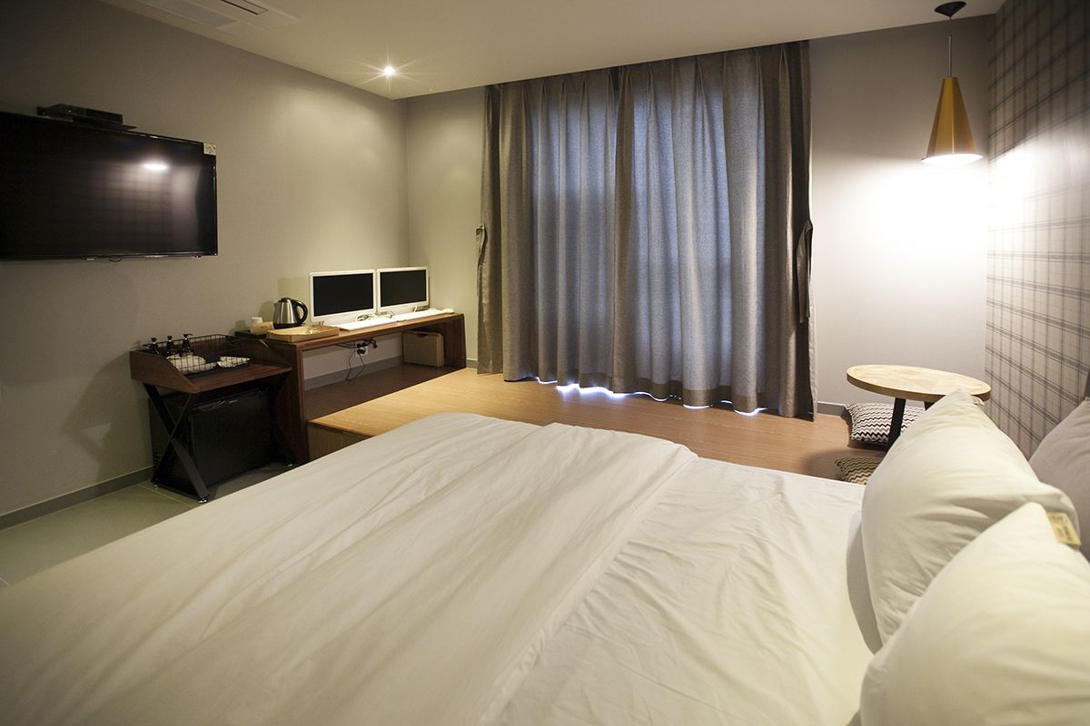 A hotel room with a large bed, a desk with two monitors, a television, and a small table.