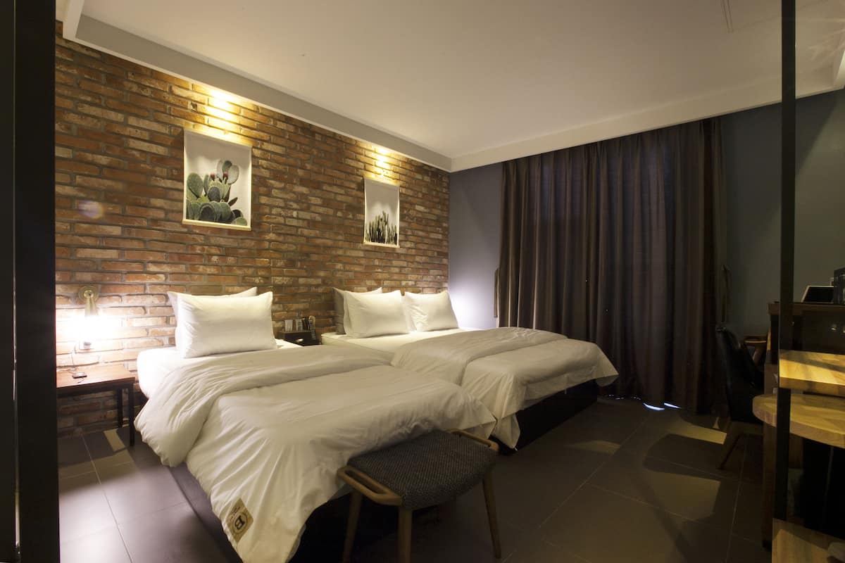 Habitación de hotel con dos camas, una pared de ladrillo decorativa, un escritorio y una silla.