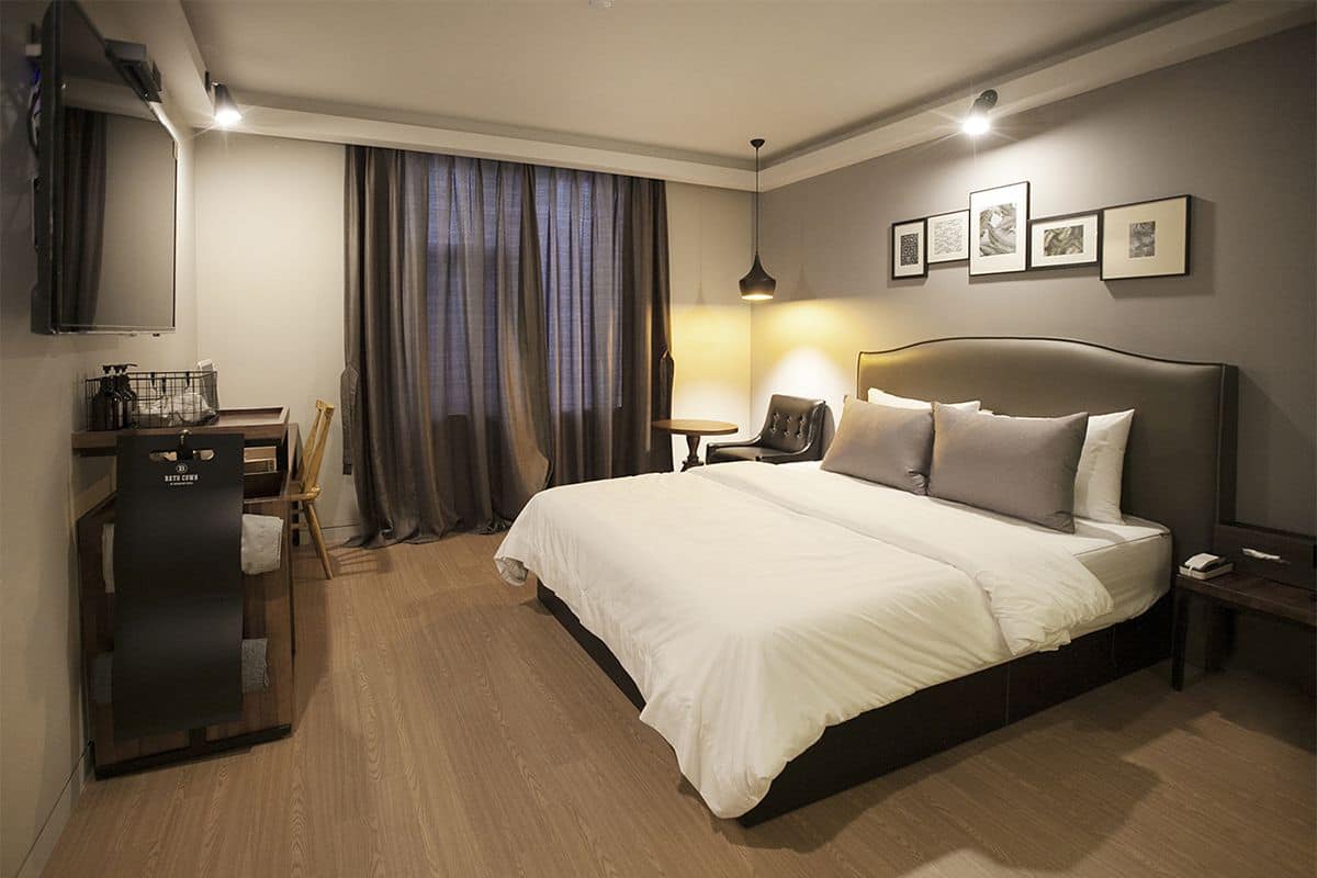 Habitación de hotel con una cama grande, un escritorio con silla, un televisor y una ventana con cortinas.