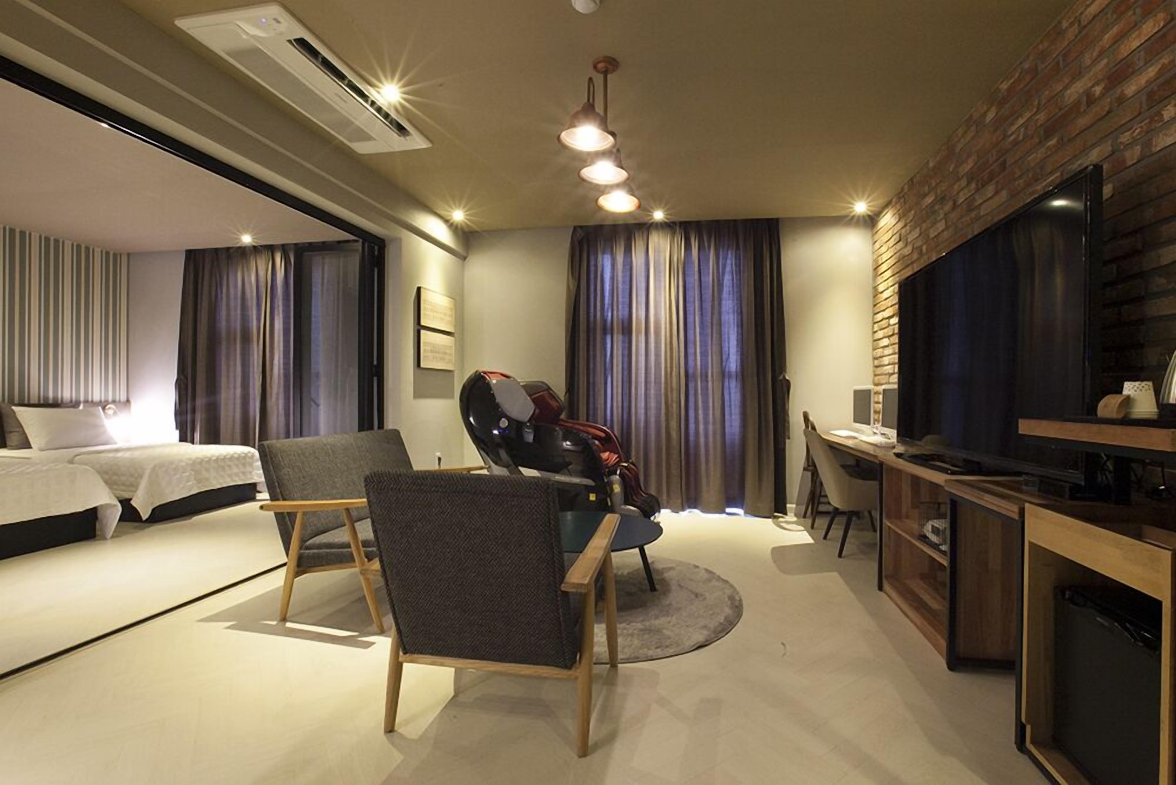 A modern hotel room with a bed, a desk, a chair, and a TV.