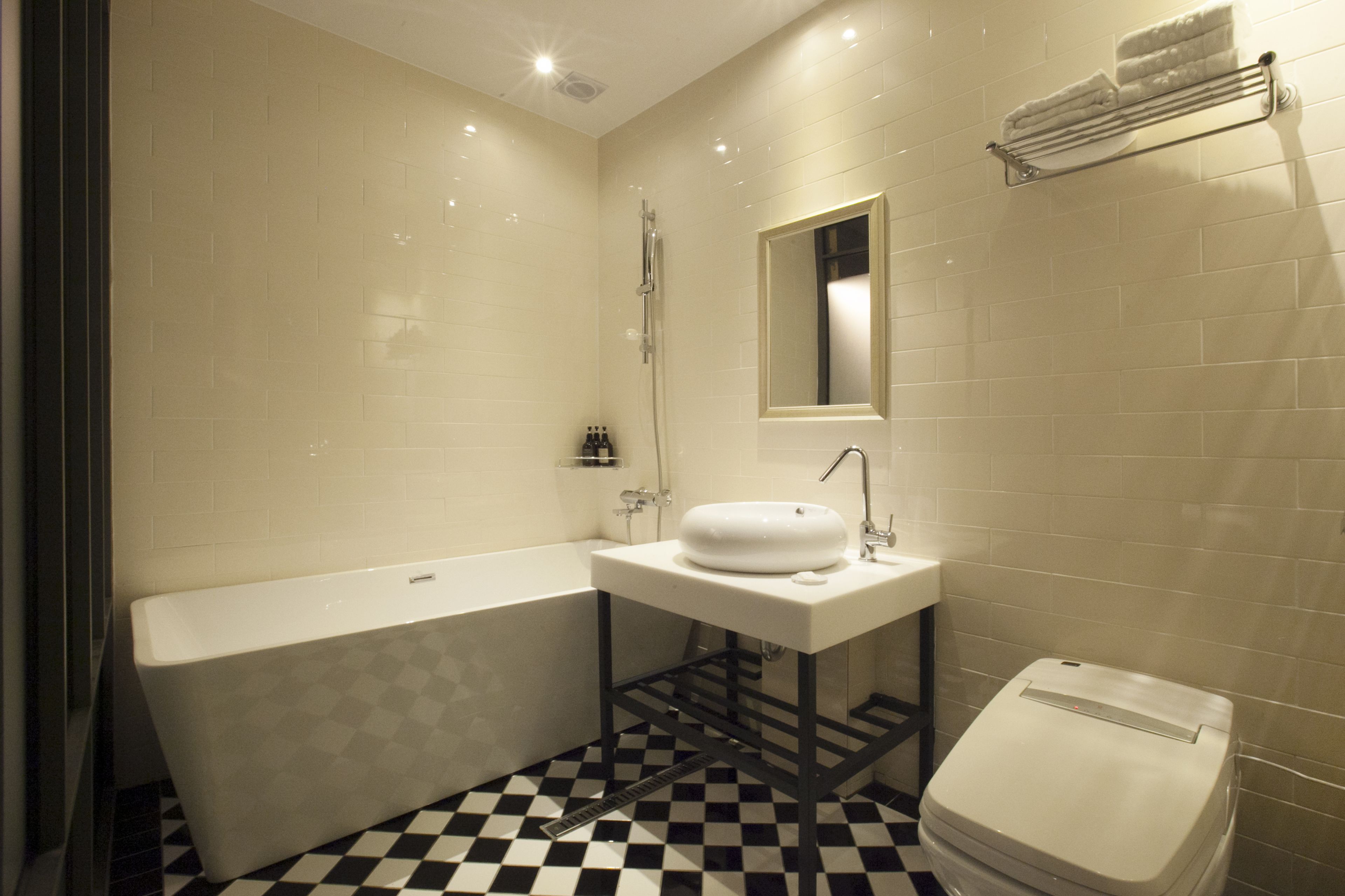 A bathroom with a checkered floor, a bathtub, a sink with a mirror above it, and a toilet.