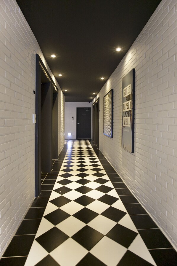 A hallway with white brick walls, a black and white checkered floor, and recessed lighting.