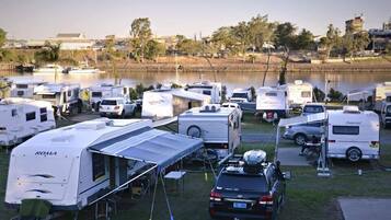 A campsite with RVs and trailers parked by a lake, with a clear view of the water and surrounding buildings.