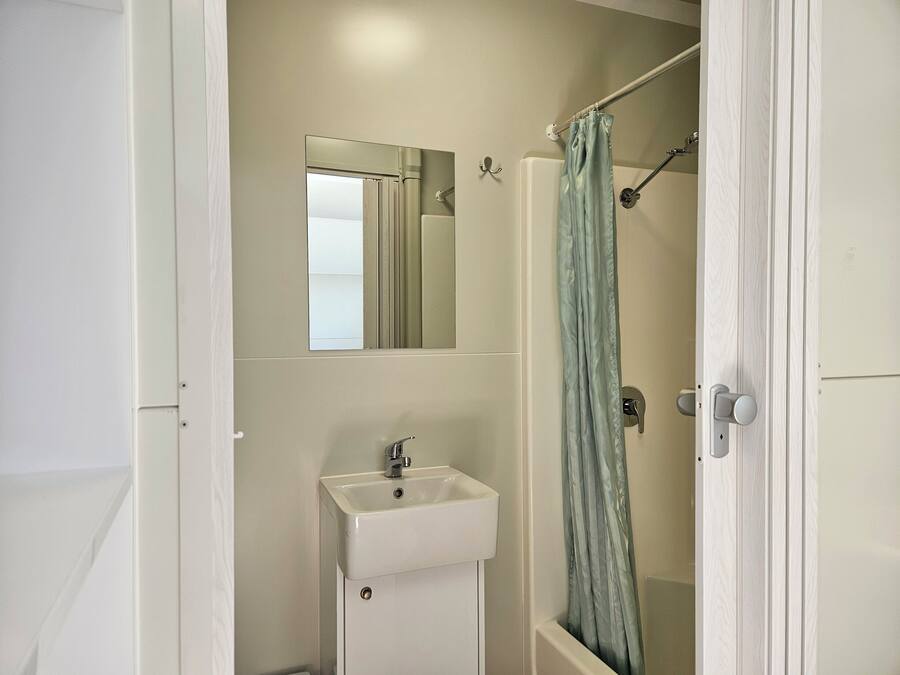 Un baño con lavamanos blanco, espejo y cortina de ducha.