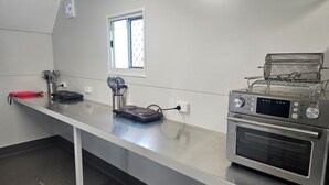 A kitchen with stainless steel countertops, a toaster, a coffee maker, and a window with blinds. - AAOK Riverdale Caravan Park (Bundaberg North)