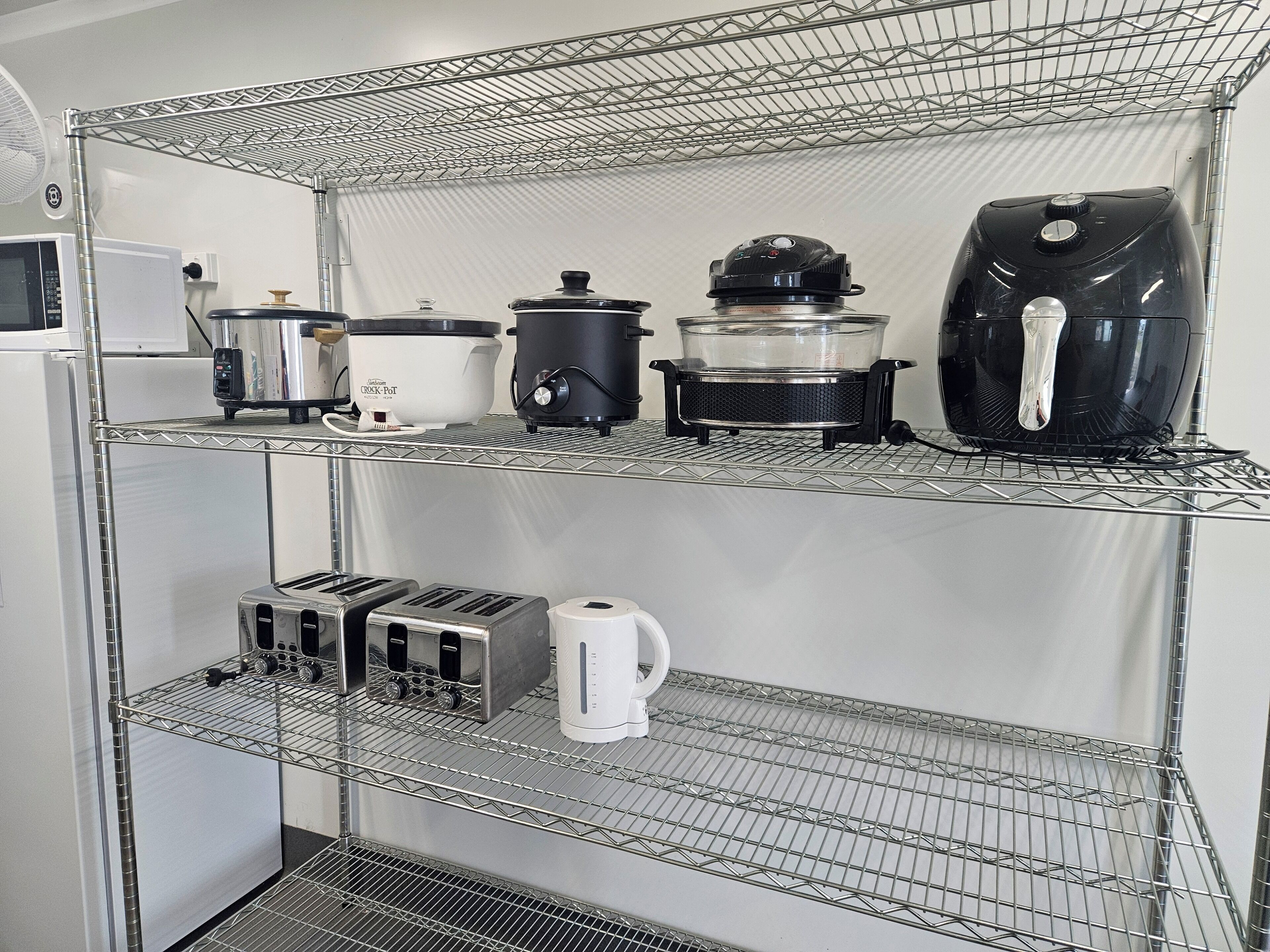Una cocina con un refrigerador, una olla de cocción lenta, una olla a presión, un tostador y una tetera sobre repisas metálicas.