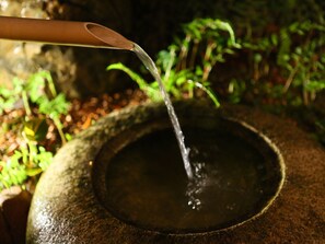 A stone water feature with a spout pouring water into a basin, surrounded by greenery. - Fukashiso (Matsumoto)