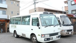 A white van parked in a residential area with a building in the background. - Fukashiso (Matsumoto)
