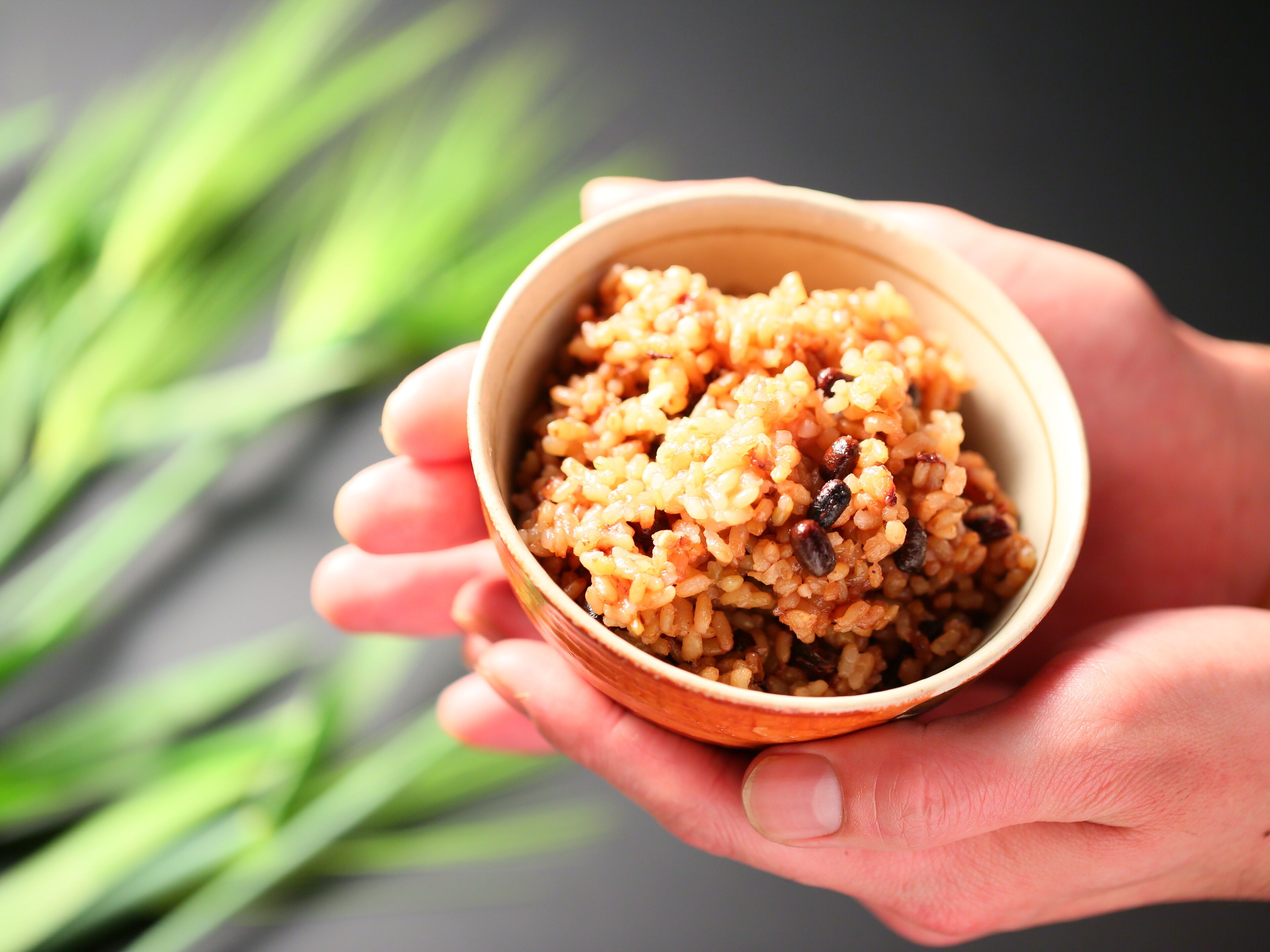 A close-up of a hand holding a bowl of rice with raisins.