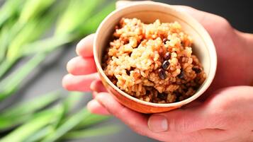 A close-up of a hand holding a bowl of rice with raisins.