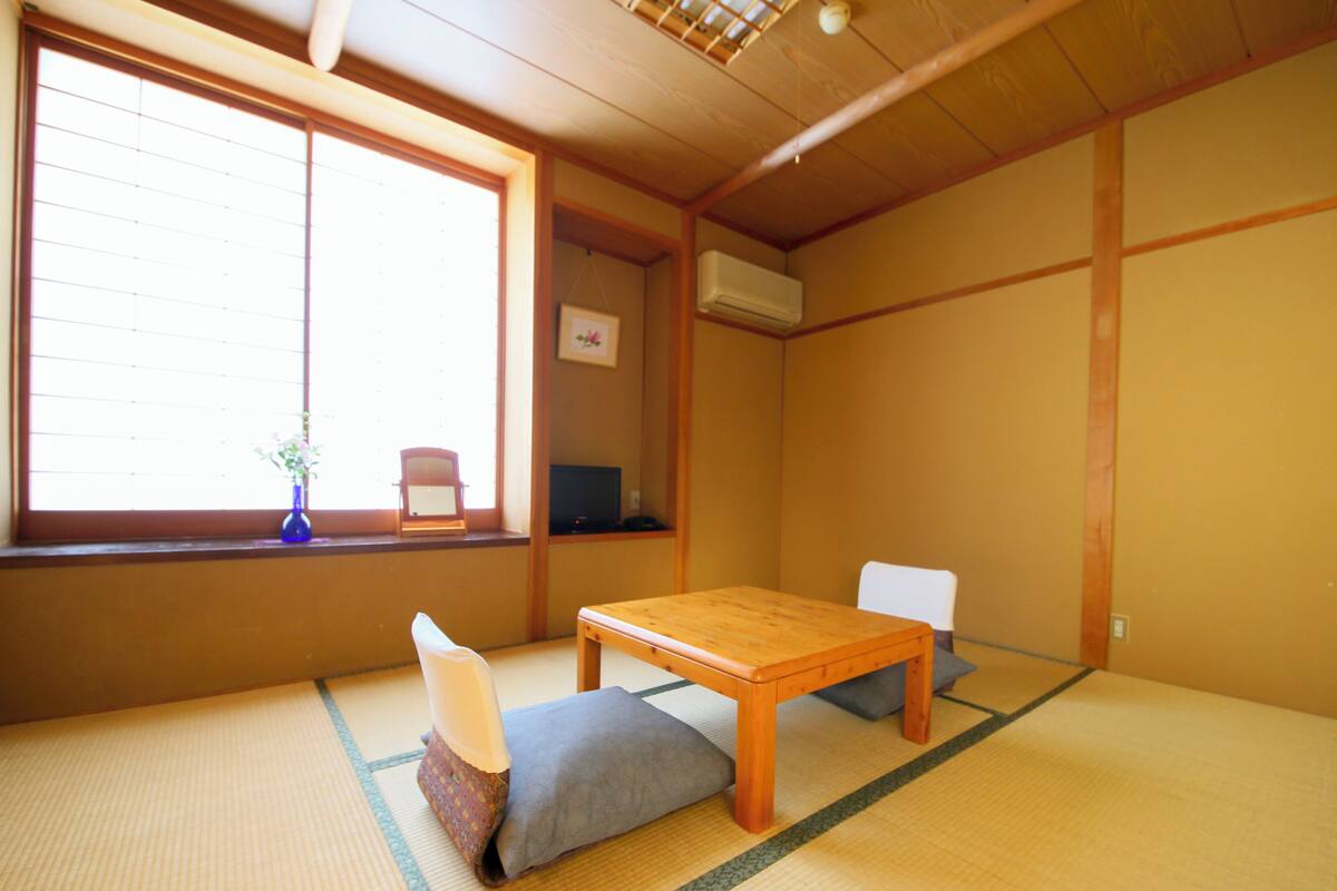 A traditional Japanese room with tatami flooring, a low wooden table, and two cushions.
